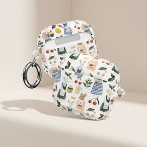 Op de afbeelding: Witte AirPod-hoes met een grillig patroon van cartoonmuizen, kersen, cupcakes en groen. De hoes is open en toont de binnenkant, en heeft een zilveren karabijnhaak. Het ontwerp is een herhalend patroon op de hoes.