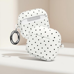 May include: Two white AirPod cases with a black polka dot design. One case is open, showing the inside. A silver carabiner clip is attached to one case. The cases are on a white surface.
