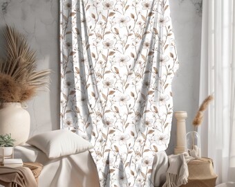 May include: White fabric curtain with a brown floral pattern. The curtain is draped over a couch with a white pillow and a brown throw blanket.