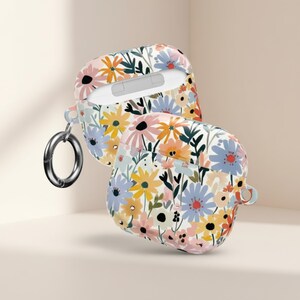 May include: AirPod case with a floral pattern in pastel colours. The case displays a variety of flowers in pink, yellow, blue, and orange, set against a white backdrop. A silver carabiner clip is attached.