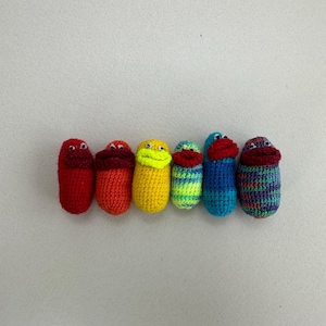 May include: A row of six crocheted finger puppets in a rainbow color pattern. The puppets are red, orange, yellow, green, blue, and purple.