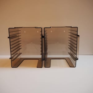 Può includere: Due portadischi in plastica trasparente colorata di marrone per CD o DVD. Ogni portadischi ha una base rettangolare e una serie di divisori orizzontali. I portadischi sono progettati per stare in posizione verticale e contenere più dischi.