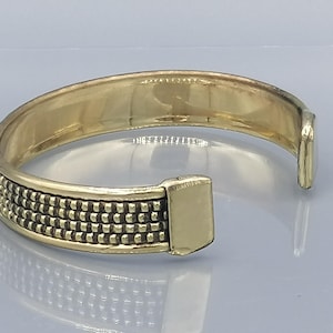 Könnte beinhalten: Ein goldfarbenes Metallarmband mit einem strukturierten Design. Das Armband hat einen Scharnierverschluss.
