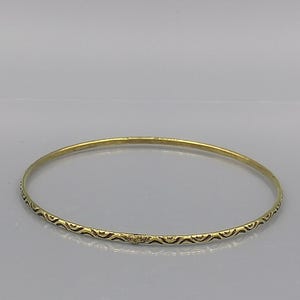 Könnte beinhalten: Ein goldenes Armreif-Armband mit einem dekorativen schwarzen Muster.