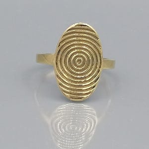Könnte beinhalten: Ein goldener Ring mit einer großen ovalen Oberseite. Die Oberseite des Rings hat ein konzentrisches Kreisdesign.
