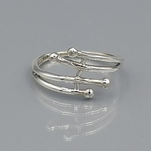 Könnte beinhalten: Ein silberner Ring mit einem einzigartigen Design aus mehreren ineinander verschlungenen Bändern und kleinen runden Akzenten.