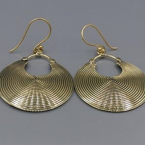 Könnte beinhalten: Ein Paar goldfarbene Ohrringe mit einem runden Design. Die Ohrringe haben ein strukturiertes, konzentrisches Kreisdesign und einen einfachen Hakenverschluss.