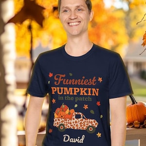 May include: A navy blue t-shirt with a graphic of a pumpkin-filled truck with a leopard print design. The text on the shirt reads "Funniest Pumpkin in the patch" and "David".