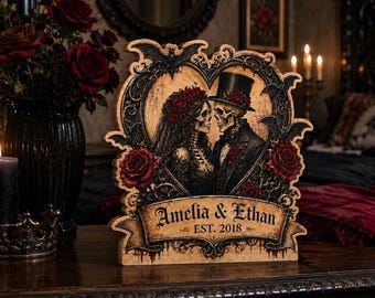 May include: A decorative wooden plaque featuring a heart-shaped frame with two skeletons dressed as a bride and groom, adorned with red roses and bats. The banner at the bottom displays the text Amelia & Ethan EST. 2018 in a dark, ornate font.