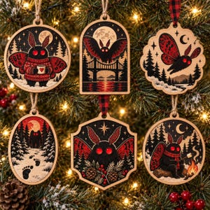 May include: A set of six wooden ornaments featuring moth-like creatures with red eyes and wings. The designs include a moth in a sweater, a moth flying over a bridge, a moth in flight, a snowy forest path with footprints, a moth with pinecones, and a moth by a campfire.
