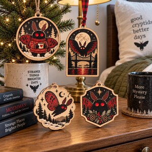 May include: Four wooden ornaments featuring moth illustrations with red eyes and black bodies. One is circular, one is arched, one is scalloped, and one is hexagonal. Each piece displays detailed forest, bridge, or moon motifs in black and red ink.