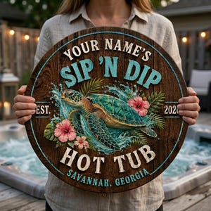 Könnte beinhalten: Ein rundes Holzschild mit dunkelbrauner Dielenoptik, das eine Meeresschildkröte im Wasser mit rosa Hibiskusblüten zeigt. Der Text lautet: YOUR NAME'S SIP 'N DIP HOT TUB, EST. 2020, SAVANNAH, GEORGIA, in hellblauer und weißer Schrift.