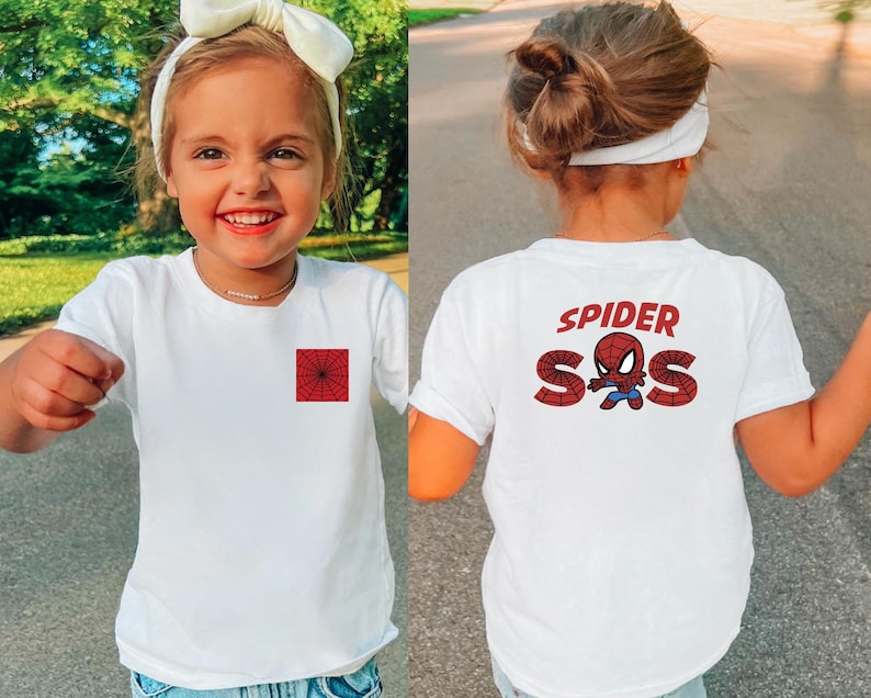 May include: White t-shirt featuring a red spiderweb square on the front and the words "SPIDER SOS" with a cartoon Spider-Man graphic on the back. The shirt is worn by a child.
