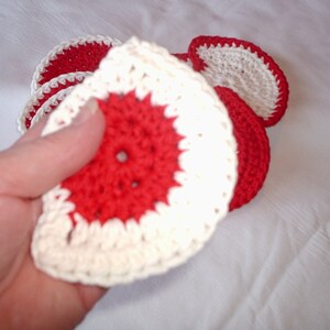 May include: A set of crocheted coasters in red and white. The coasters are round and have a scalloped edge.