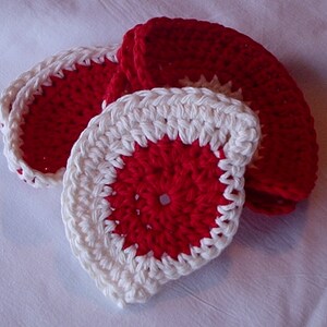 May include: Set of four crocheted coasters in red and white. The coasters are circular and have a raised center.