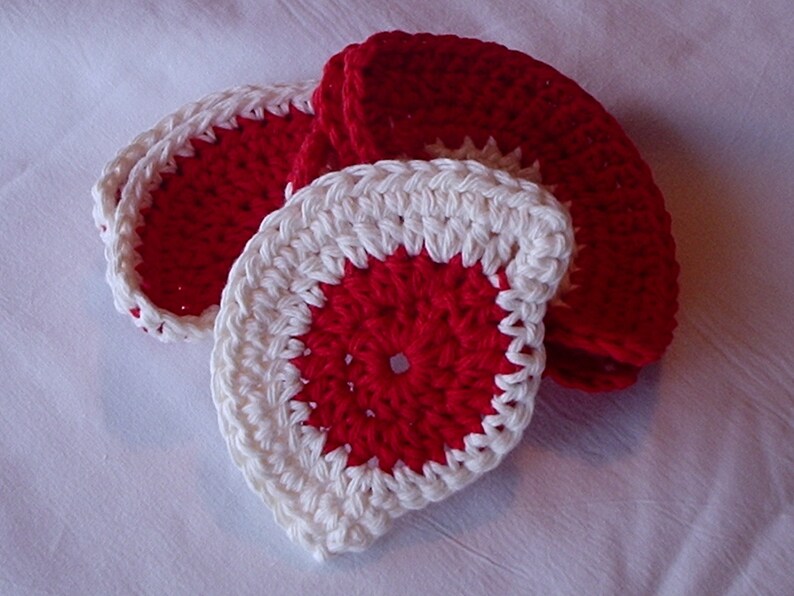 May include: Set of four crocheted coasters in red and white. The coasters are circular and have a raised center.