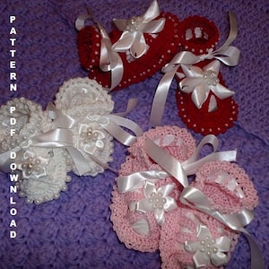 Puede incluir: Tres pares de botines de bebé de ganchillo con lazos de cinta de satén blanco y adornos de perlas. Los botines son de color blanco, rosa y rojo.