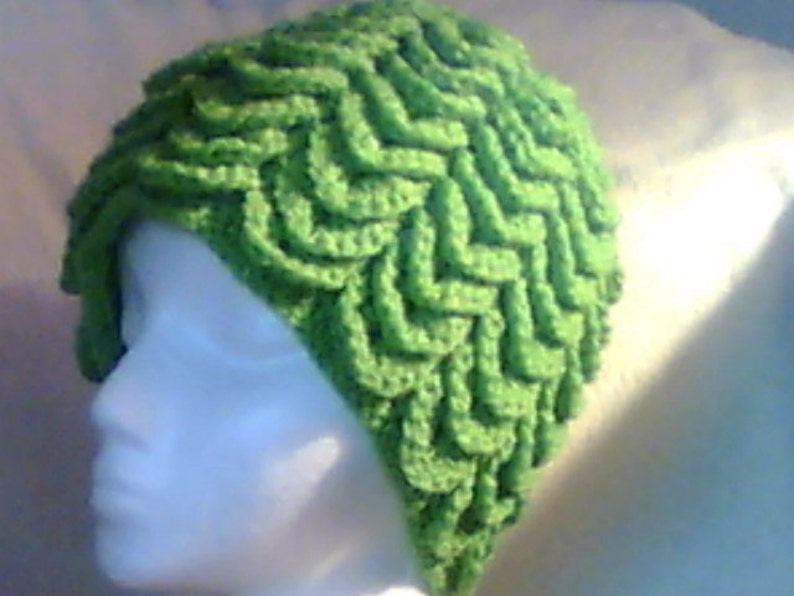 May include: A bright green crocheted hat with a textured, wave-like pattern. The hat is made of soft yarn and has a unique, eye-catching design. This handmade hat is a stylish accessory.
