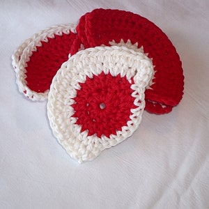 May include: Set of four crocheted coasters in red and white. The coasters are round and have a scalloped edge.
