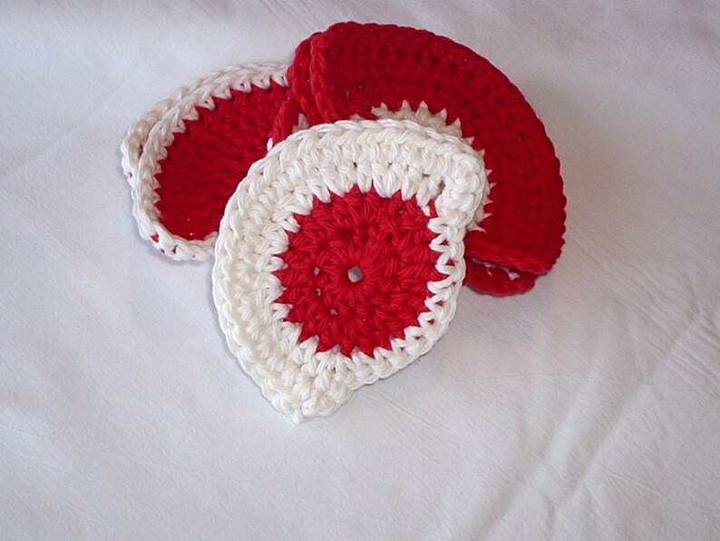 May include: Set of four crocheted coasters in red and white. The coasters are round and have a scalloped edge.