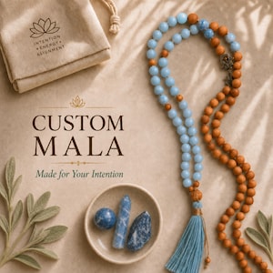 Puede incluir: Un collar mala con cuentas azul claro y marrones con una borla azul, acompañado de una pequeña bolsa beige con cordón y un cuenco de cerámica que contiene una esfera azul, una punta de cristal azul y un fragmento de piedra azul. Texto: CUSTOM MALA.