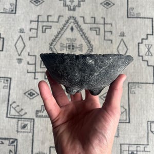 May include: A small, black, three-legged bowl made of ceramic.