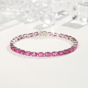 Może przedstawiać: Srebrna bransoletka z rzędem owalnych, jaskraworóżowych kamieni szlachetnych. Kamienie są osadzone blisko siebie, tworząc ciągłą linię koloru. Bransoletka jest prezentowana na białej powierzchni, z miękkim oświetleniem.