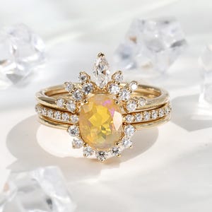 Può includere: Un set di tre anelli d'oro. L'anello centrale presenta una gemma ovale gialla circondata da piccole pietre trasparenti. L'anello superiore ha una pietra taglio marquise. Gli anelli sono su sfondo bianco.