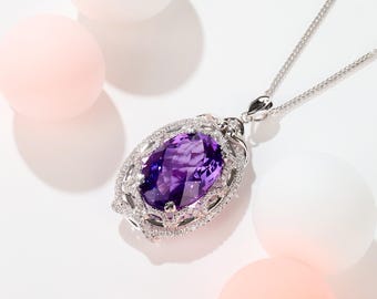 May include: A silver necklace with a large, oval-cut purple amethyst pendant. The pendant is surrounded by a halo of small, clear gemstones. The necklace is on a white surface with pink and white spheres.