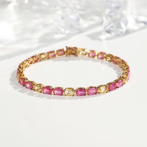 May include: A gold bracelet featuring alternating oval-cut pink and yellow gemstones. The bracelet is displayed on a white surface, with soft lighting highlighting the jewellery's sparkle. A classic and elegant piece.