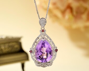 May include: A silver necklace with a pear-shaped amethyst pendant surrounded by smaller diamonds and red gemstones.