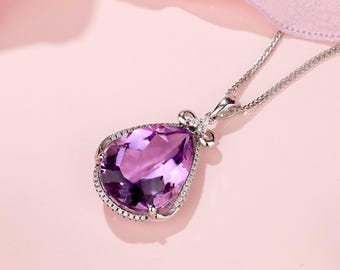May include: A silver necklace with a teardrop-shaped amethyst pendant surrounded by smaller diamonds. The pendant is set in a silver frame with a bow detail at the top.