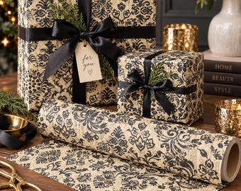 Puede incluir: Dos cajas de regalo rectangulares y un rollo de papel de regalo con un patrón de damasco negro sobre un fondo beige texturizado. Las cajas están envueltas con cinta de satén negra, adornadas con ramas verdes y una tiene una etiqueta for you.