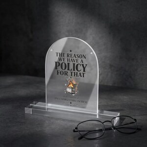 May include: An arched clear acrylic plaque with a rectangular base featuring black text that reads THE REASON WE HAVE A POLICY FOR THAT and IN RECOGNITION OF ONE UNFORGETTABLE INCIDENT, with a graphic of a burning dumpster in the centre.