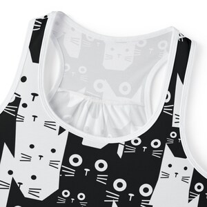 May include: A white and black tank top with a cat face pattern. The cat faces are stylized with large eyes, whiskers, and a small "T" for the nose. The tank top has a racerback design and a white trim.