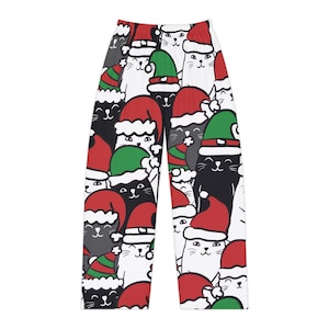 Op de afbeelding: Pyjamabroek met een herhalend patroon van zwarte, witte en grijze cartoonkatten die rode en groene kerstmutsen dragen. Het feestelijke ontwerp bedekt het hele kledingstuk en toont verschillende uitdrukkingen van katten en kerstmutsen.