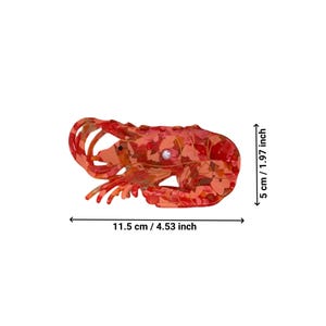 Pode incluir: Um prendedor de cabelo em forma de lagosta vermelho e laranja com um detalhe de p&eacute;rola. O prendedor mede 11,5 cm de largura e 5 cm de altura.