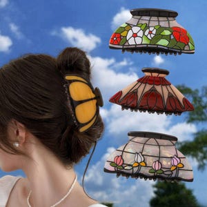 Peut inclure: Un ensemble de quatre pinces à cheveux. L'une est en forme de papillon jaune portée dans des cheveux foncés. Trois autres présentent des motifs de style vitrail : une avec des fleurs rouges et blanches, une avec des tulipes rouges et une avec des lotus.