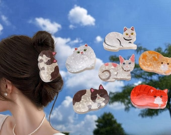 May include: A set of 7 cat-shaped hair clips. The clips are made of resin and have a sparkly finish. The cats are in various poses, including sleeping, sitting, and standing. The clips are in a variety of colors, including white, pink, orange, and brown.