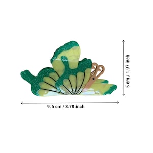 May include: A green and yellow butterfly-shaped hair clip with a glittery finish. The clip measures 3.78 inches wide and 1.97 inches tall.