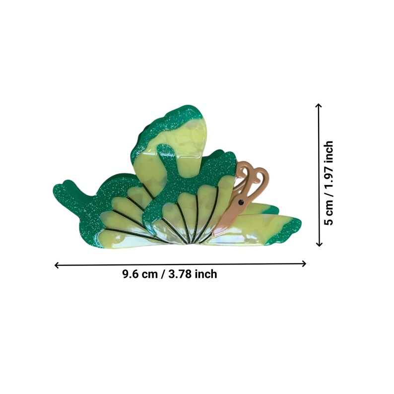May include: A green and yellow butterfly-shaped hair clip with a glittery finish. The clip measures 3.78 inches wide and 1.97 inches tall.