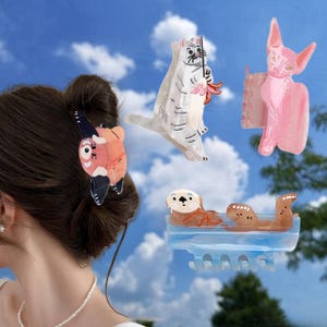 May include: A collection of four hair clips featuring animal designs: a red panda, a white cat with a toy, a pink hairless cat, and an otter floating in blue water. Each clip is made of a glossy material with detailed, colorful illustrations.