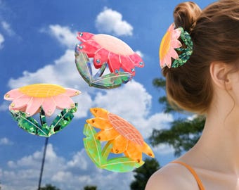 Könnte beinhalten: Eine Sammlung von Haarspangen in Form von Blumen in Rosa, Gelb und Orange. Jede Spange hat ein Blumendesign mit Blütenblättern und grünen Blättern. Eine Spange ist im Haar einer Frau, die anderen schweben vor blauem Himmel.