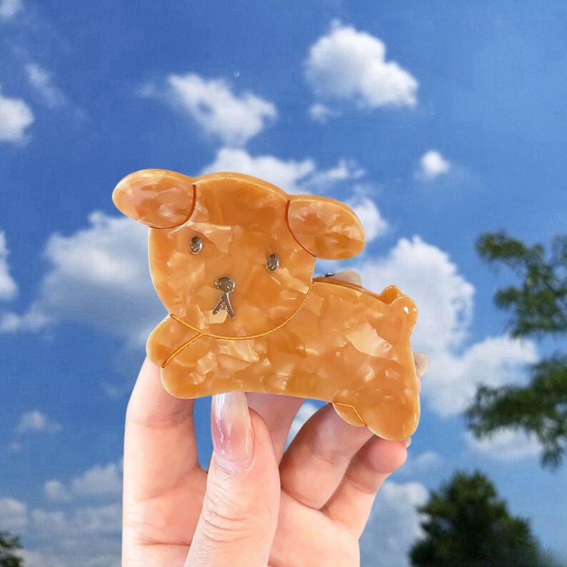 May include: A brown and white marbled plastic hair clip shaped like a cartoon dog. The dog has a small, black nose and eyes.