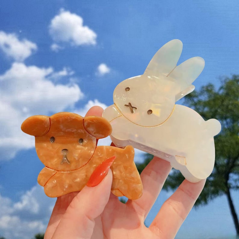 May include: Two plastic hair clips shaped like a rabbit and a puppy. The rabbit clip is white and the puppy clip is brown.