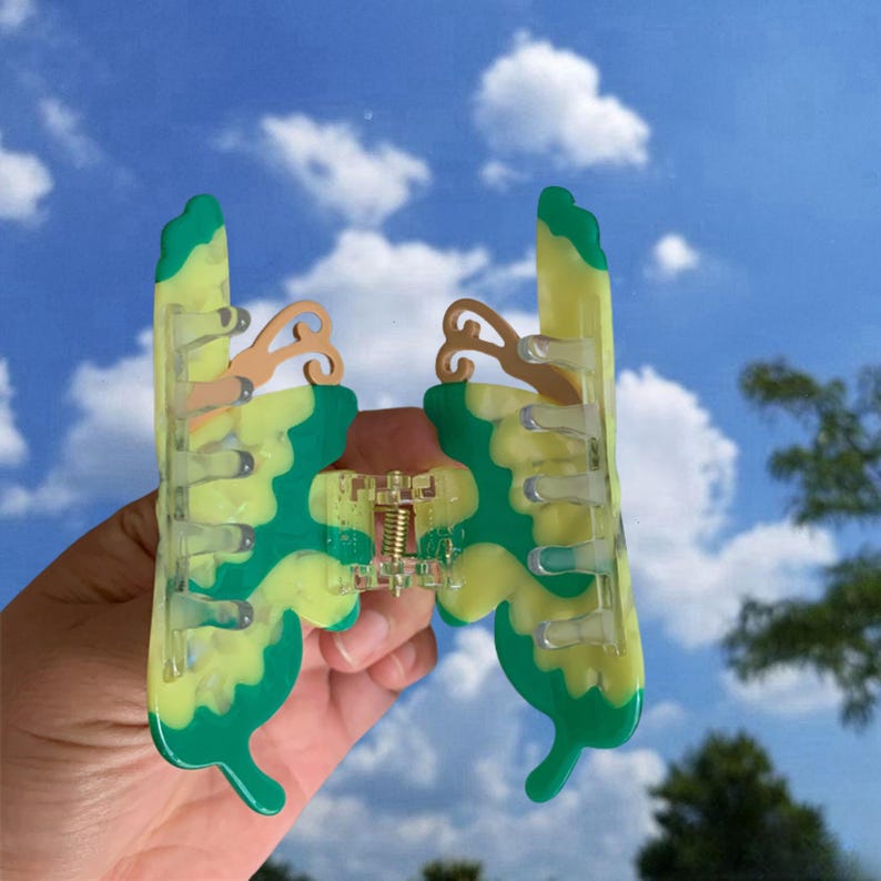 May include: A green and yellow butterfly-shaped hair clip with a clear plastic clasp. The clip has a wavy design and is made of plastic.