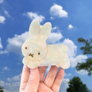 May include: A white iridescent plastic bunny rabbit hair clip. The bunny is laying down with its head turned to the side. The bunny has a brown nose and eyes.