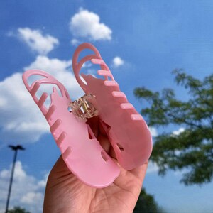 Pode incluir: Uma presilha de cabelo de pl&aacute;stico rosa com um design ondulado &uacute;nico. A presilha est&aacute; aberta e pronta para segurar o cabelo.