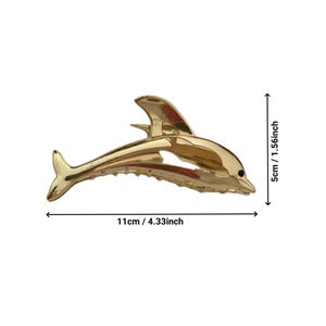Puede incluir: Una pinza para el pelo de color dorado en forma de delf&iacute;n, que mide 11 cm de largo y 4 cm de alto.