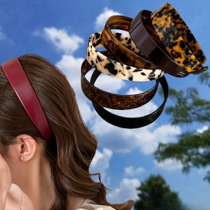 Pode incluir: Uma coleção de seis tiaras, incluindo uma faixa lisa na cor bordô usada na cabeça e cinco faixas empilhadas com vários padrões, como casco de tartaruga, preto e um design manchado em branco e preto, todas com acabamento liso.